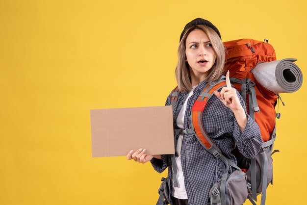 mujer viajera con mochila sosteniendo cartón dedo apuntando hacia arriba