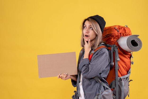 Mujer viajera pensativa con mochila roja sosteniendo cartón