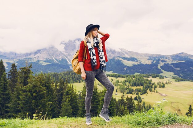 Mujer viajera con sombrero y mochila disfrutando de increíbles vistas a la montaña