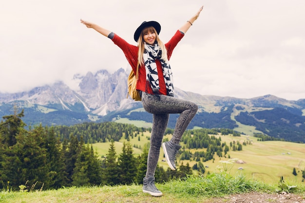 Mujer viajera con sombrero y mochila disfrutando de increíbles vistas a la montaña