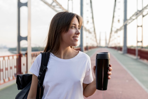 Foto gratuita mujer viajera sonriente sosteniendo termo en puente