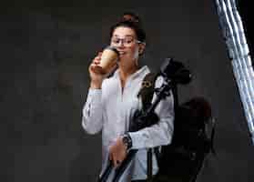 Foto gratuita la mujer viajera sostiene una cámara fotográfica digital y café para llevar sobre fondo gris.