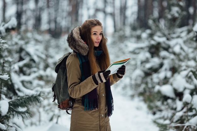 Mujer de viajero con mapa en sus manos en el bosque de invierno cubierto de nieve. Concepto de viaje