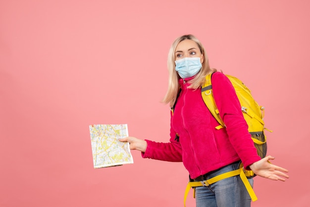 Mujer de viajero de vista frontal con mochila amarilla con mapa de explotación de máscara médica