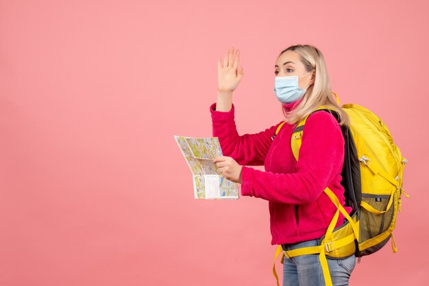 Mujer de viajero de vista frontal con mochila amarilla con máscara agitando la mano