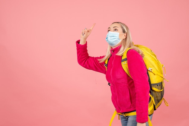 Mujer de viajero de vista frontal con mochila amarilla con máscara apuntando al techo