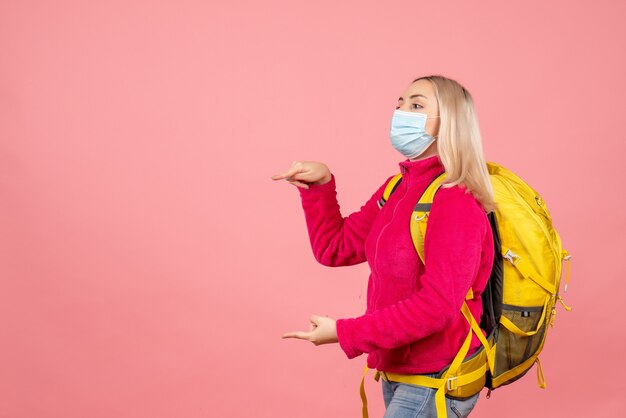 Mujer de viajero de vista frontal con mochila amarilla con máscara apuntando a la izquierda