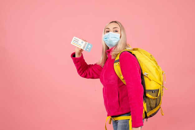 Mujer de viajero de vista frontal con mochila amarilla con máscara sosteniendo el boleto