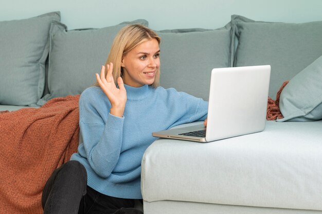 Mujer con una videollamada en casa en una computadora portátil y saludando durante la pandemia