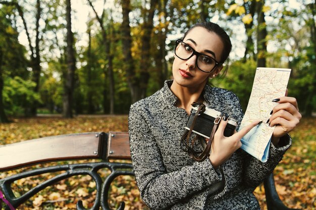 La mujer en vidrios grandes se coloca con la cámara y un mapa turístico