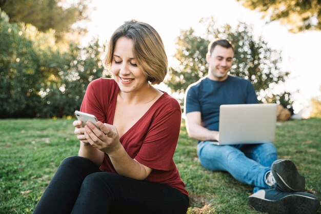 Mujer viendo el teléfono inteligente cerca del hombre con la computadora portátil