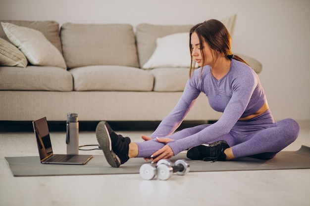 Mujer viendo tutoriales y entrenando desde casa en una alfombra usando cuerda para saltar y pesas