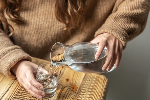 Una mujer vierte agua en un vaso de una jarra de vidrio