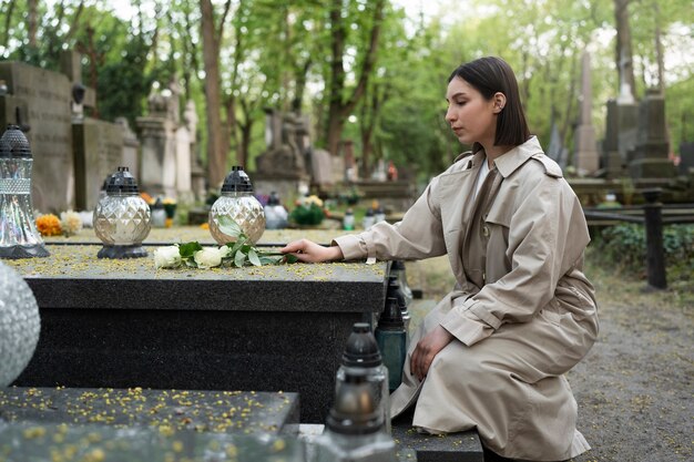 Mujer visitando una tumba en el cementerio y trayendo flores.