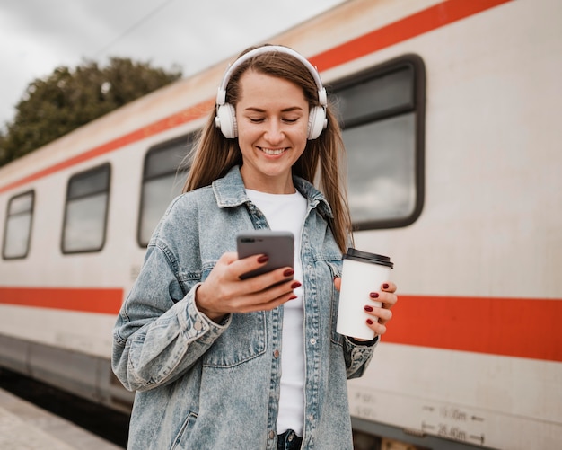 Mujer de vista frontal escuchando música en la estación de tren