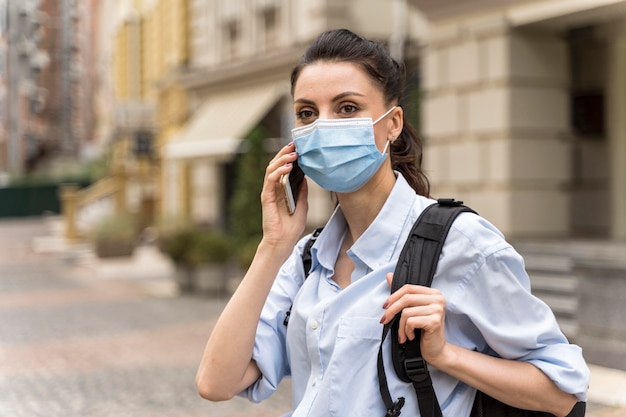 Mujer de vista frontal hablando por teléfono con una mascarilla en