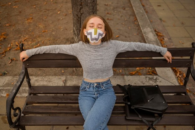 Foto gratuita mujer de vista frontal con máscara médica sentada en un banco