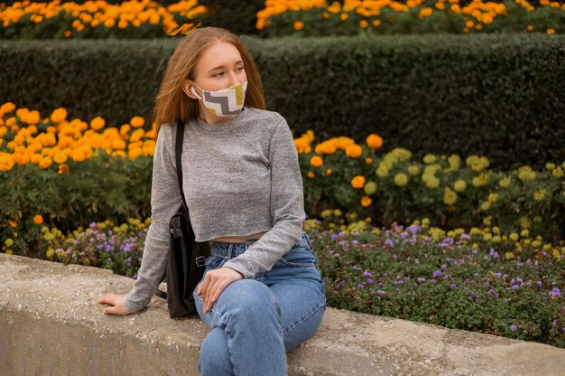 Mujer de vista frontal con máscara médica sentado junto a un jardín