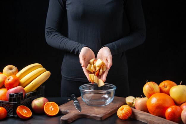 Mujer de vista frontal poniendo rodajas de manzana fresca en un tazón de frutas en bandeja de madera en la mesa