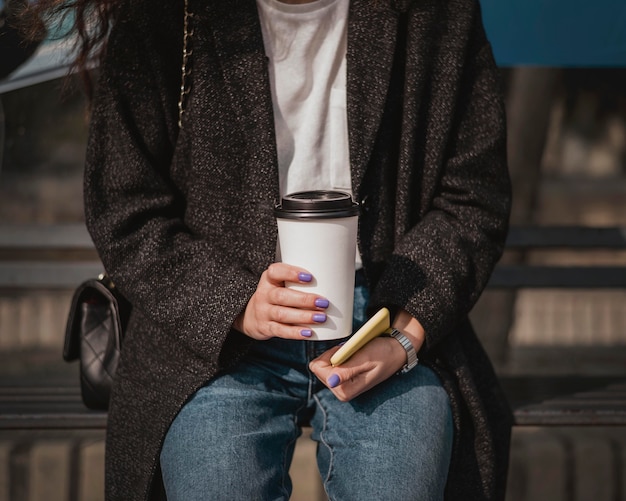 Foto gratuita mujer de vista frontal sosteniendo un café y esperando el autobús