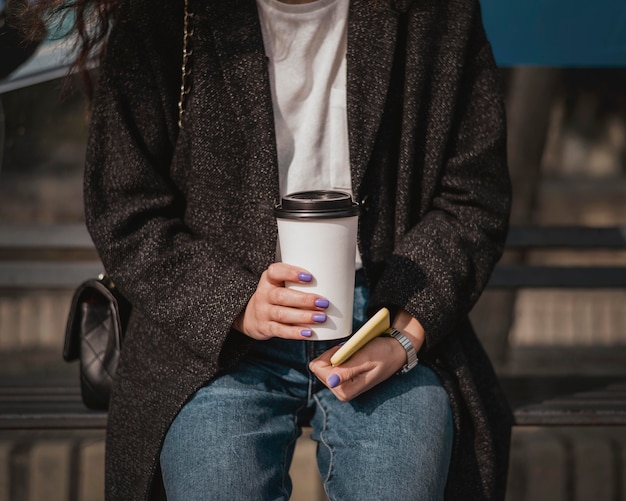 Mujer de vista frontal sosteniendo un café y esperando el autobús