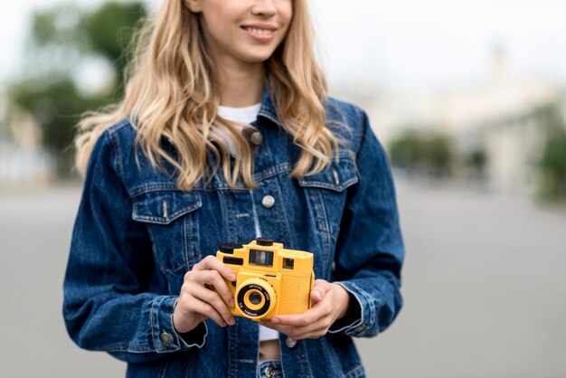 Mujer de vista frontal sosteniendo una cámara amarilla retro