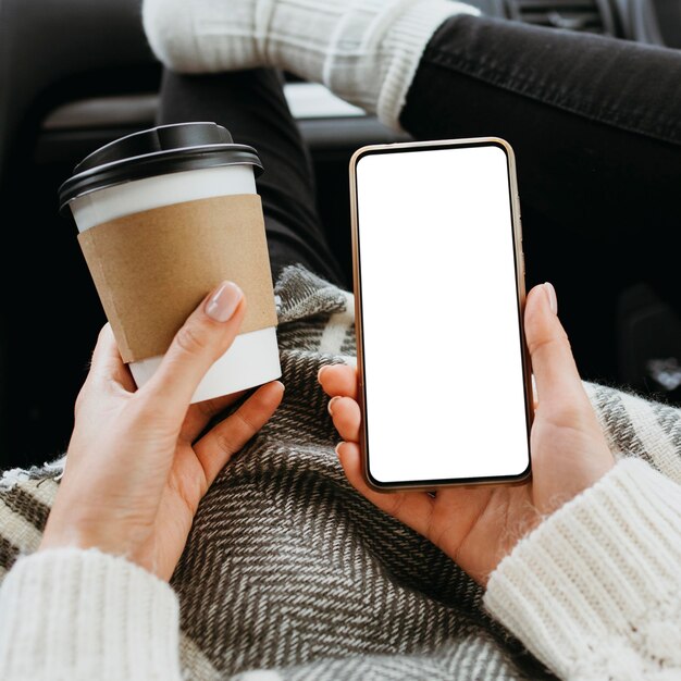 Mujer de vista frontal sosteniendo un teléfono en blanco y una taza de café