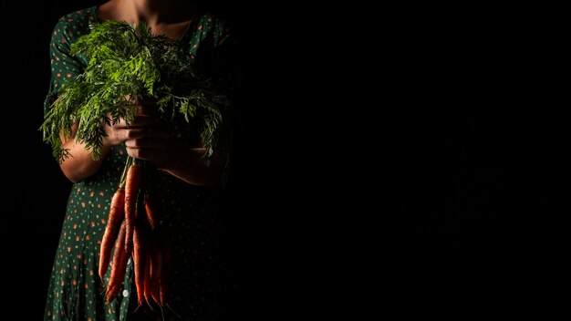 Mujer de vista frontal sosteniendo zanahorias con espacio de copia