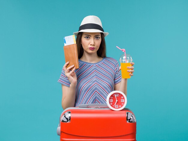 Mujer de vista frontal en vacaciones sosteniendo boletos y jugo en el fondo azul viaje de vacaciones viaje por mar viaje femenino