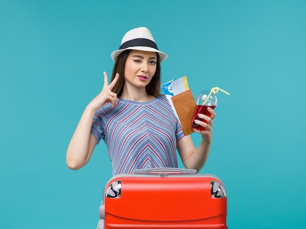 Mujer de vista frontal en vacaciones sosteniendo jugo con boletos sobre fondo azul claro viaje de viaje femenino mar avión de verano