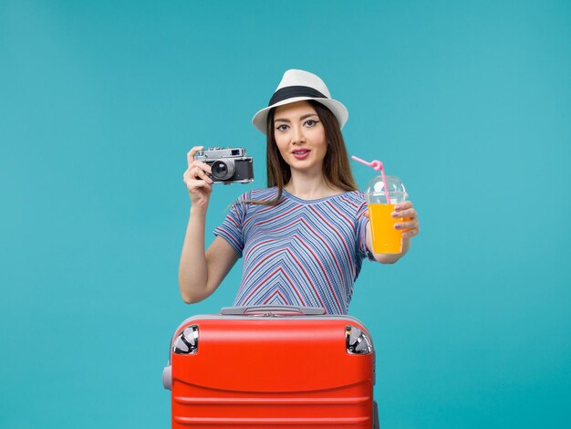 Mujer de vista frontal en vacaciones sosteniendo jugo y cámara en el fondo azul claro viaje viaje de verano viaje vacaciones mar