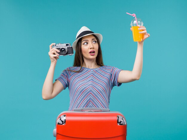 Mujer de vista frontal en vacaciones sosteniendo jugo y cámara en el fondo azul viaje por mar viaje de verano viaje vacaciones