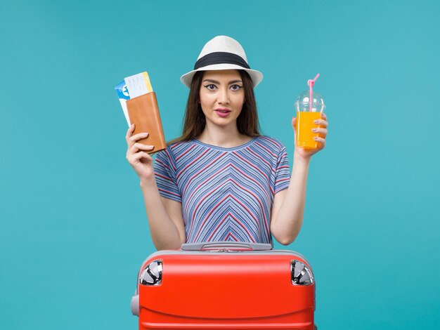 Mujer de vista frontal en vacaciones sosteniendo su jugo y boletos sobre fondo azul viaje verano viaje por mar viaje vacaciones