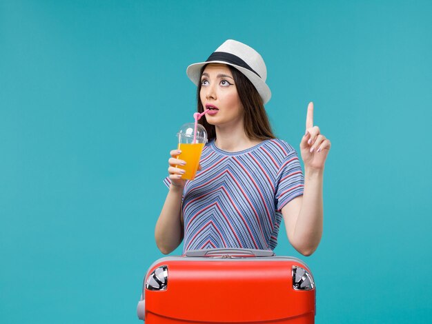 Mujer de vista frontal en vacaciones con su bolsa roja sosteniendo su jugo sobre fondo azul claro viaje verano mar viaje viaje vacaciones