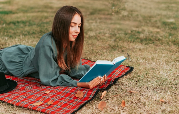 Mujer de vista lateral leyendo un libro sobre una manta de picnic