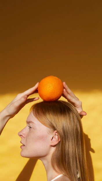 Mujer de vista lateral posando con naranja