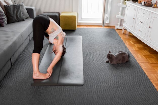 Mujer de vista lateral practicando yoga y gato en casa