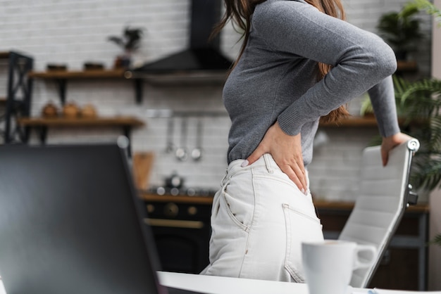 Mujer de vista lateral que tiene dolor de espalda mientras trabaja desde casa