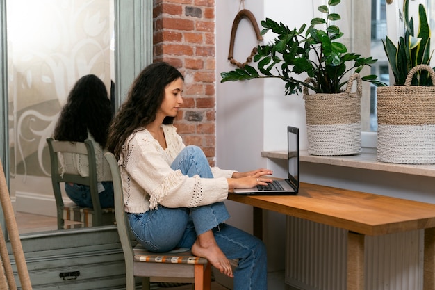 Mujer de vista lateral que trabaja en la computadora portátil en casa