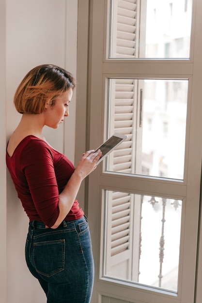 Foto gratuita mujer de vista lateral que usa la tableta junto a la ventana