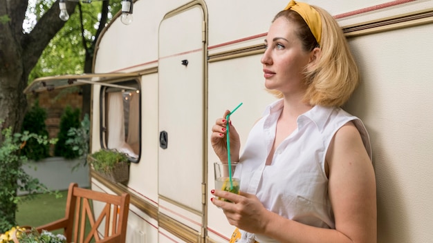 Mujer de vista lateral sosteniendo un vaso de limonada junto a una caravana