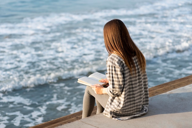 Mujer de vista posterior leyendo junto al mar