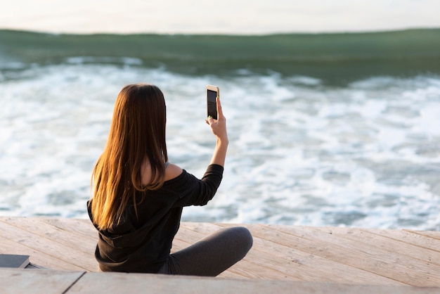 Mujer de vista posterior tomando una foto del mar