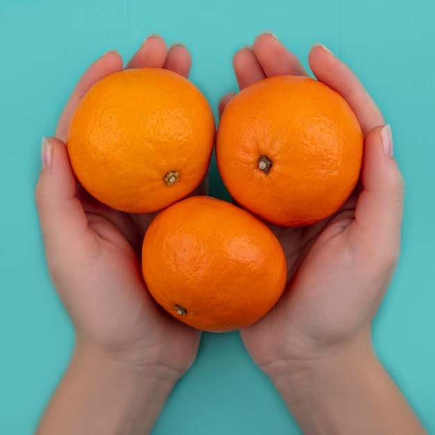 Mujer de vista superior sosteniendo naranjas en sus manos sobre un fondo turquesa