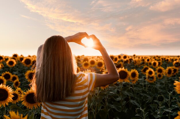 Mujer de vista trasera haciendo manos en forma de corazón en una puesta de sol