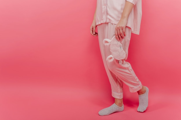 La mujer viste un acogedor camisón de algodón de pie sobre una pared rosa. Retrato de modelo de mujer en pijama y calcetines grises.