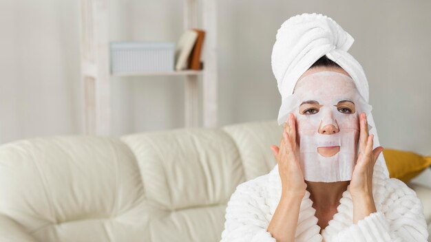 Mujer vistiendo albornoz y aplicando mascarilla facial