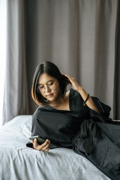 Mujer vistiendo una camisa negra acostada en la cama y jugando smartphone.