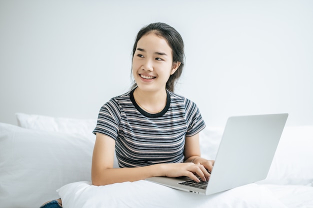 Una mujer vistiendo una camisa a rayas en la cama y jugando felizmente portátil.