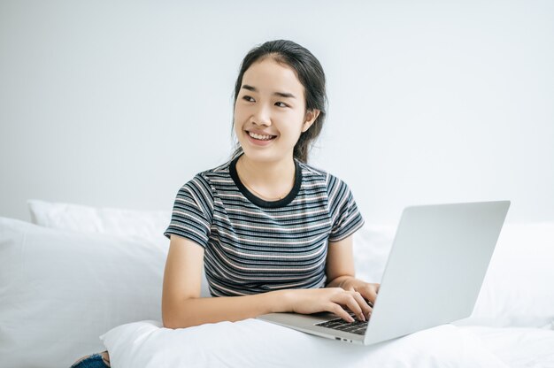 Una mujer vistiendo una camisa a rayas en la cama y jugando felizmente portátil.